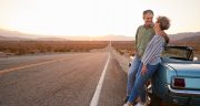 Senior couple on road trip standing by car, full length