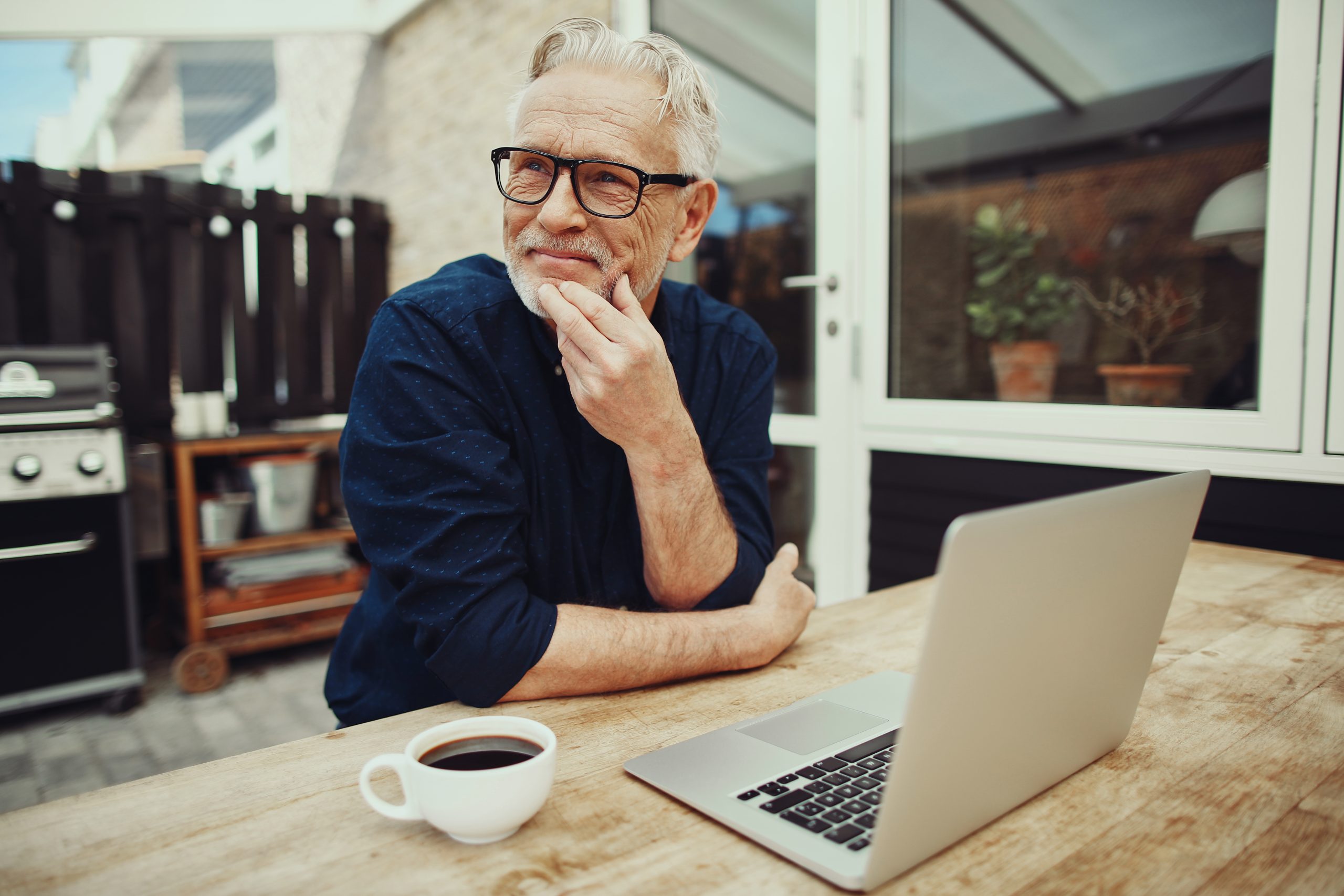 Senior man sitting outside drinking coffee and using a laptop